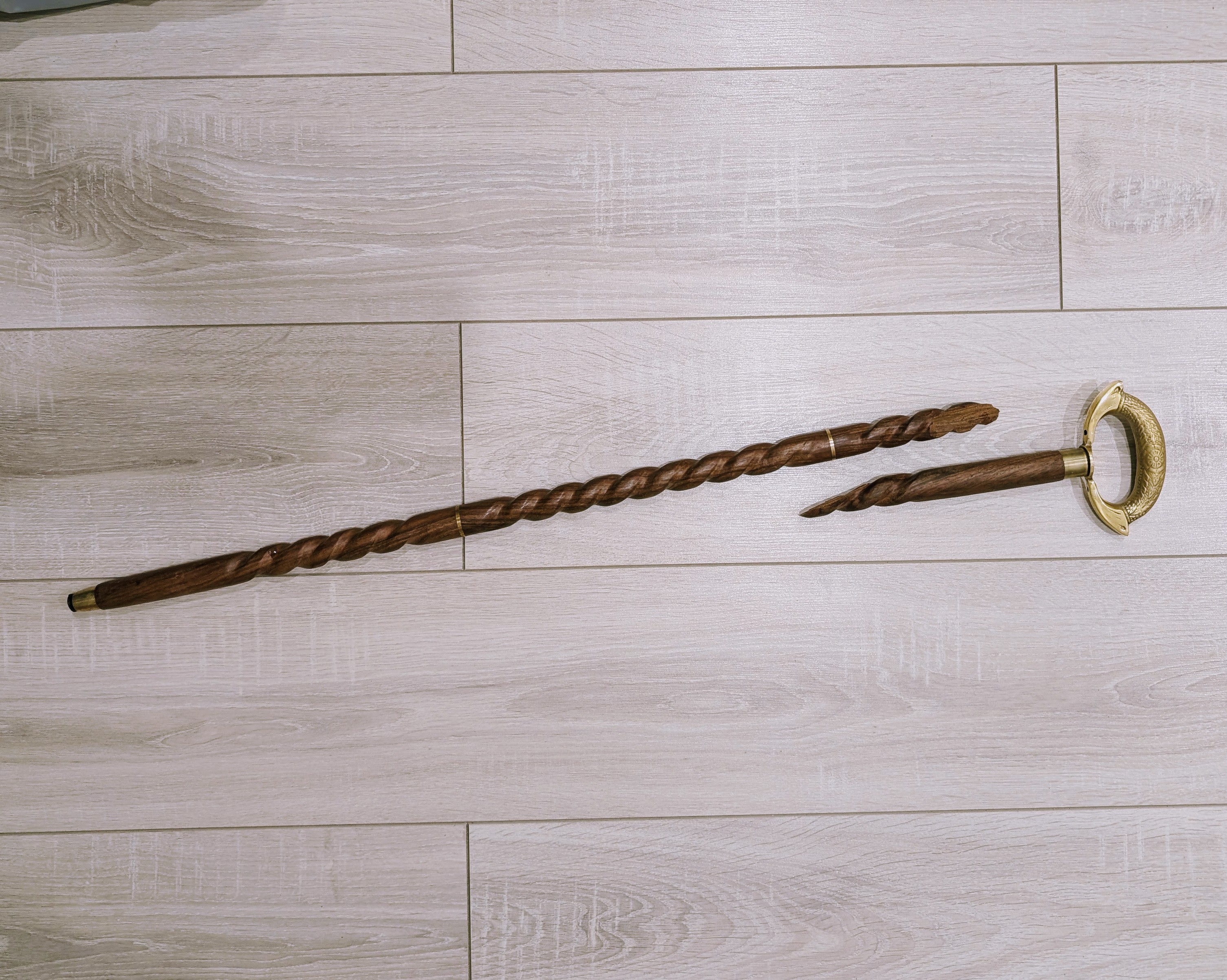 The carved wooden cane after the snap, lying on the floor in two pieces with a diagonal break