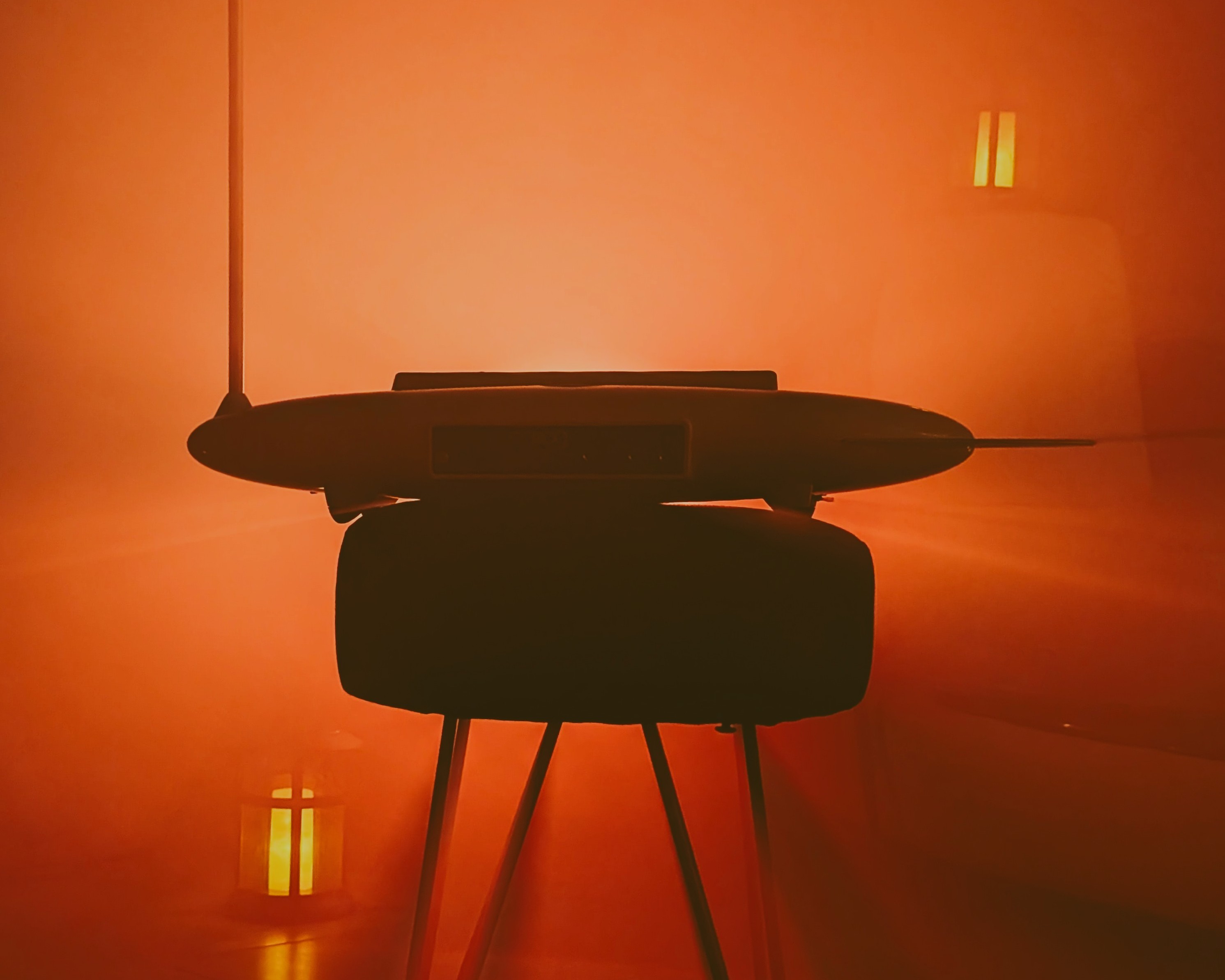 The theremin silhouetted on its stand inside dense orange fog, with ambient lanterns glowing on either side