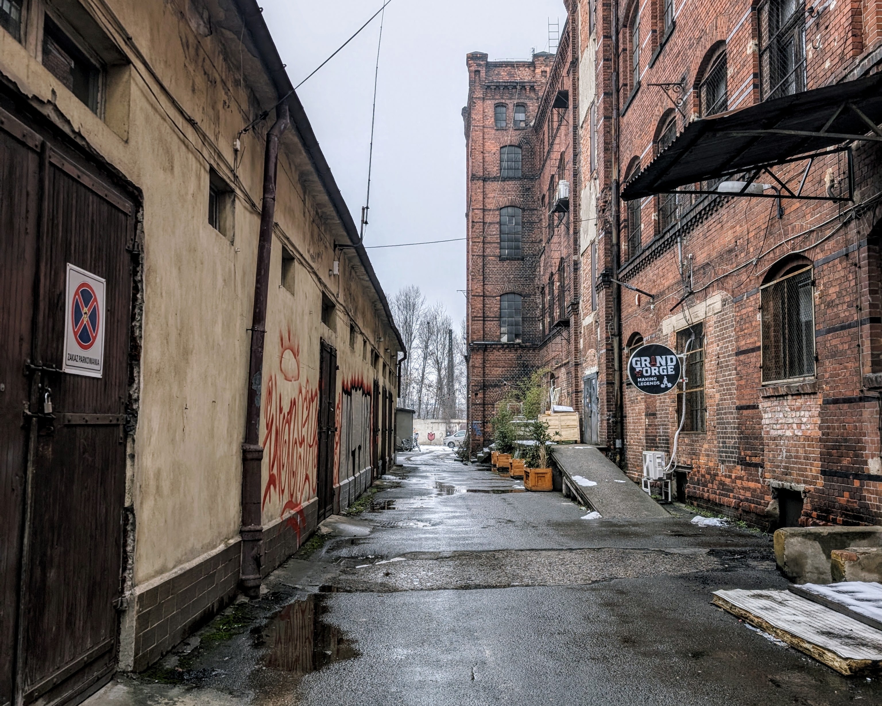 The back alley in Wrocław leading to Weronika's studio, with wet asphalt and an old red-brick building